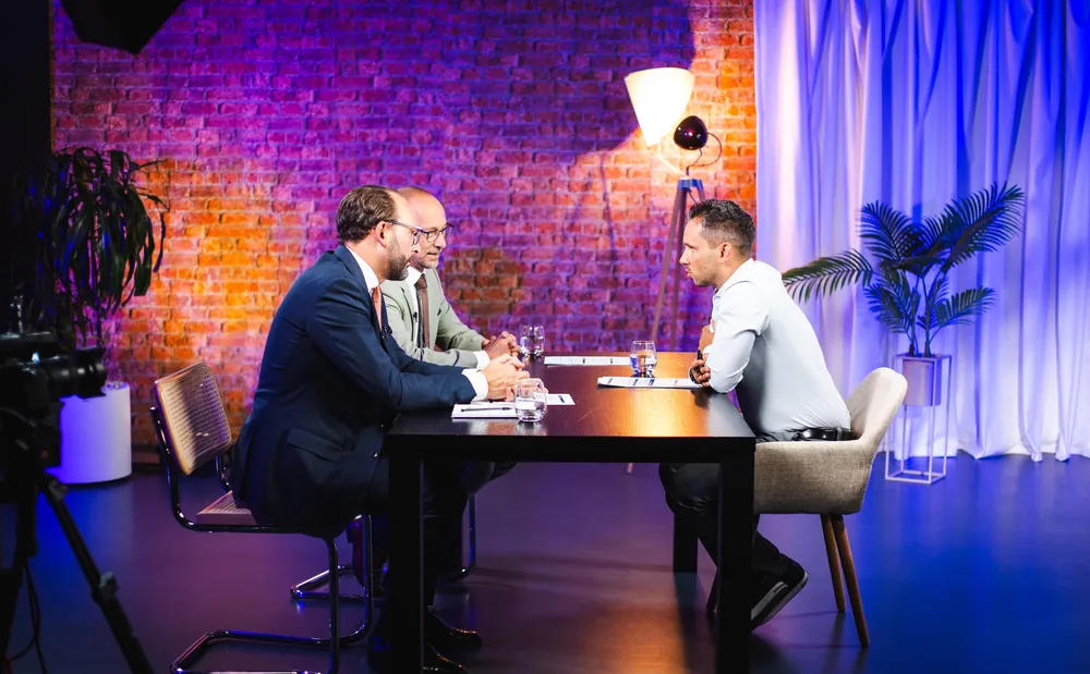 Interviewtisch vor Backsteinwand und blauem Vorhang mit drei Personen
