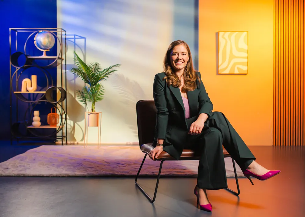 Farbenfrohes Set mit Regal, Globus und oranger Wand, Frau im Anzug auf einem Sessel