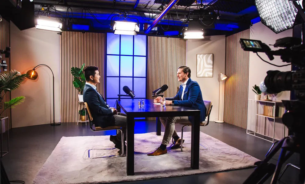 Interview mit Tisch, Holzlamellen und blauem Fensterelement, Kamera im Vordergrund